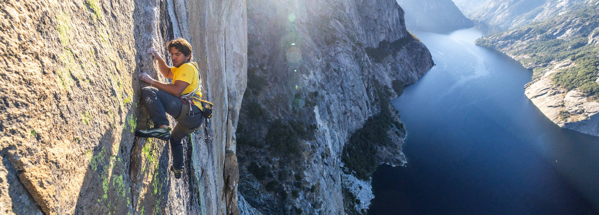 Person climbing a steep cliff with a scenic view of a lake and mountains in the background