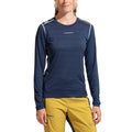 A person wearing a navy blue La Sportiva Tour Long Sleeve Women’s (2025) shirt—crafted from recycled polyester—and yellow pants, stands facing forward with a slight smile and hands by their sides, showcasing this comfortable winter layer.