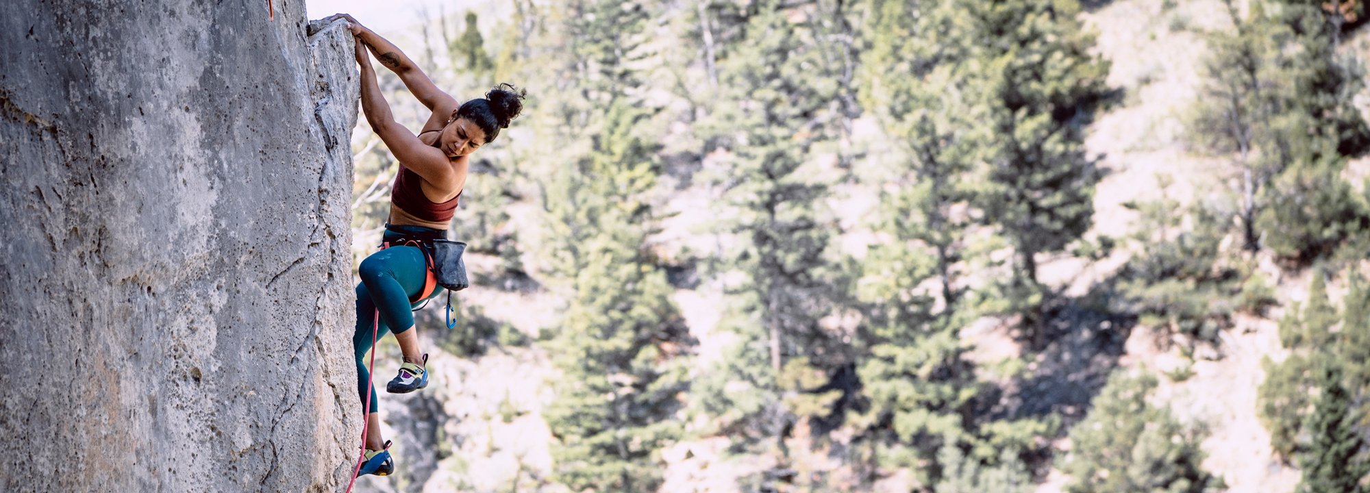 Person climbing a rocky cliff with trees in the background