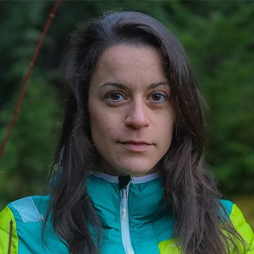 Woman wearing a green and yellow jacket outdoors with a blurred natural background