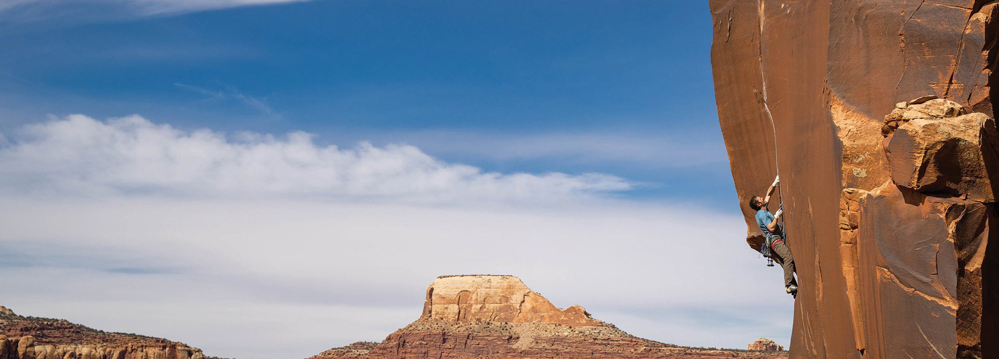 Person climbing a rock face with a scenic landscape in the background