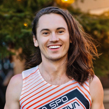 Person with long hair smiling outdoors with trees in the background