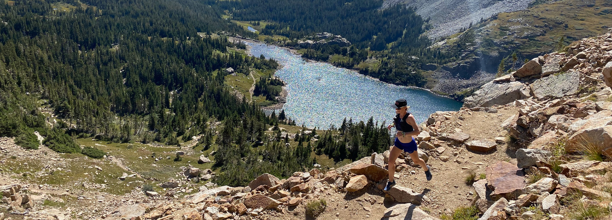 Person running on a rocky trail with a scenic mountain lake view