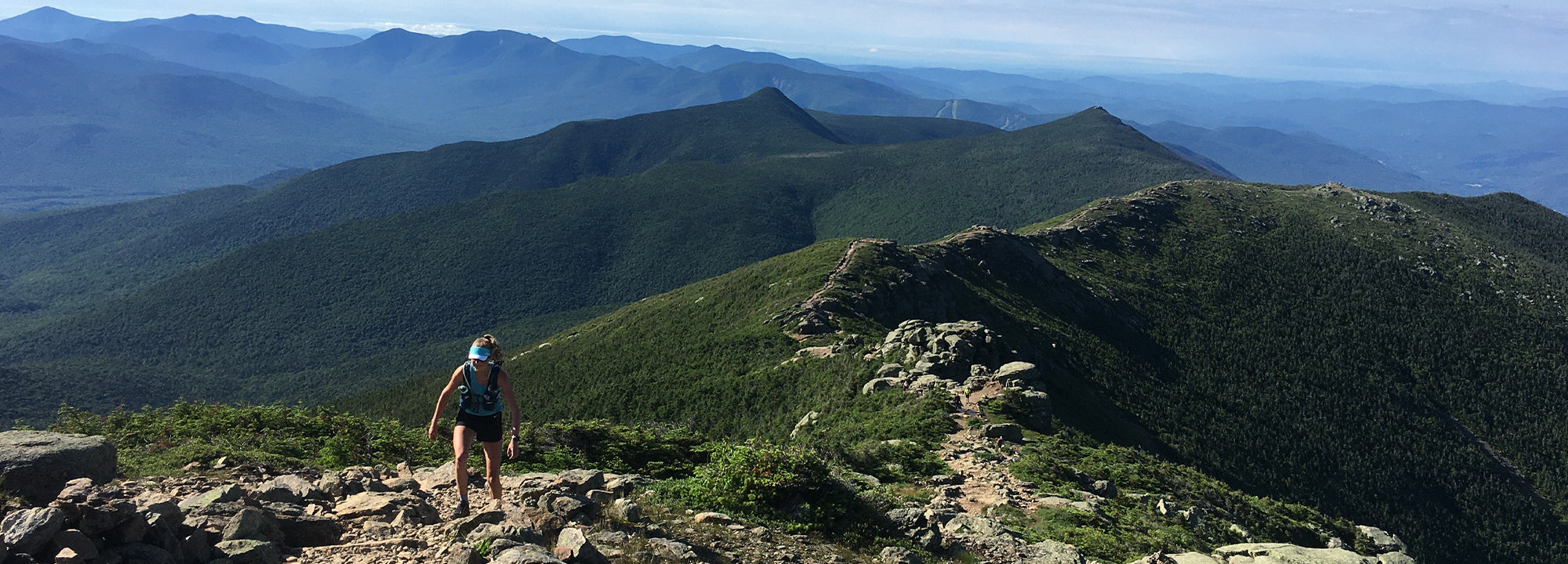 Person standing on a mountain peak with a scenic view of mountains in the background