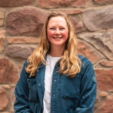 Person wearing a blue jacket in front of a stone wall