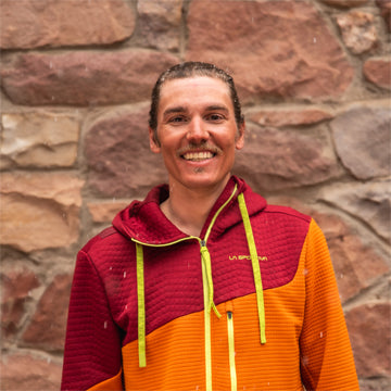 Person wearing a red and orange jacket with a visible brand logo against a stone wall.