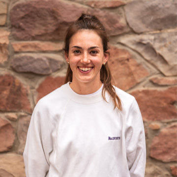 Person wearing a white sweatshirt with a logo against a stone wall background
