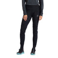 A person is shown from the waist down wearing La Sportiva’s Primal Pants Women’s—black thermal pants designed for winter running—paired with a dark long-sleeve top and black trail shoes with light blue soles, standing against a white background.