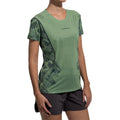 Une femme portant le T-shirt La Sportiva Pacer Women's en camouflage vert, fabriqué à partir de polyester recyclé, l'associe à un short d'athlétisme noir et se tient debout sur un fond blanc uni.