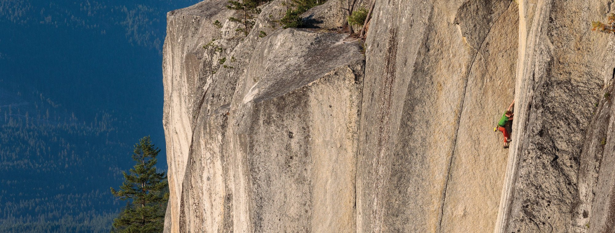 Person climbing a steep cliff face with a clear blue sky above.
