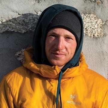Person wearing a yellow jacket with a brand logo against a textured wall.