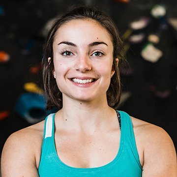 Woman in a teal tank top smiling in front of a climbing wall.