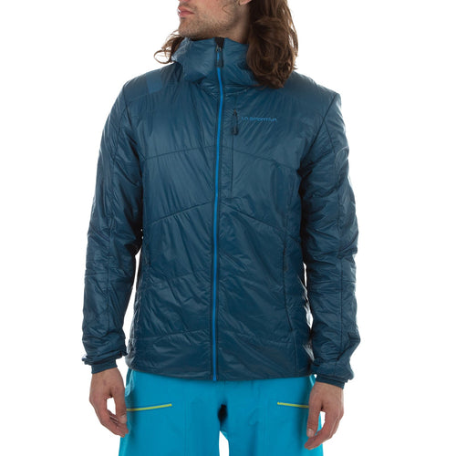Un homme vêtu d'une veste La Sportiva Alpine Guide Primaloft Hoody Men's (2024) bleu sarcelle avec col montant et poche de poitrine zippée, et d'un pantalon bleu vif, se tient légèrement tourné sur un fond blanc uni. La veste est légère et respirante.