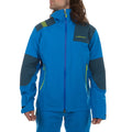 A person wears the La Sportiva Roseg GTX Jacket Men's in bright blue with dark gray accents and green zippers. The hardshell features a high collar and hood, partially covering their face beneath long brown hair.