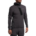 Un homme porte le La Sportiva Big Wall Pullover Hoody Men's (2025) en gris foncé, avec des manches longues, un col montant, une poche sur la poitrine et un tissu TechStretch Aero avec des inserts en Polartec, associé à un short gris assorti.