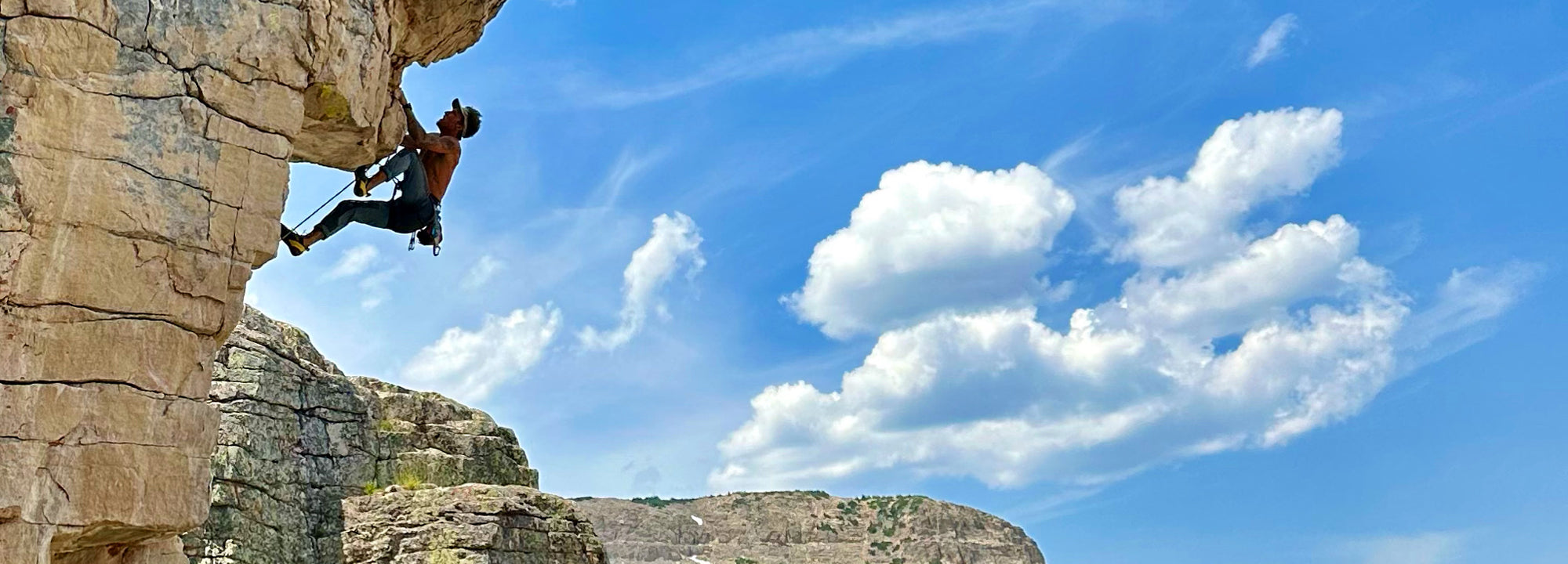 Person climbing a rocky cliff with a clear blue sky and clouds in the background
