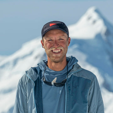 Man wearing a cap and jacket with mountains in the background