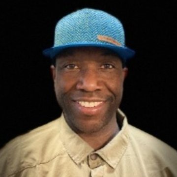 Person wearing a blue cap and beige jacket against a black background