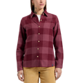 Une femme portant la chemise en flanelle Rambler de La Sportiva pour femme, au motif à carreaux rouges et roses et dotée de boutons en noix de coco, la porte par-dessus un t-shirt blanc et l'associe à un pantalon en velours côtelé beige, debout, face à l'objectif, devant un fond blanc uni.