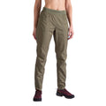 A person wearing La Sportiva Roots Pants Women's in olive green with articulated knees, elastic waistband, and front pockets, along with maroon hiking shoes, stands against a white background.