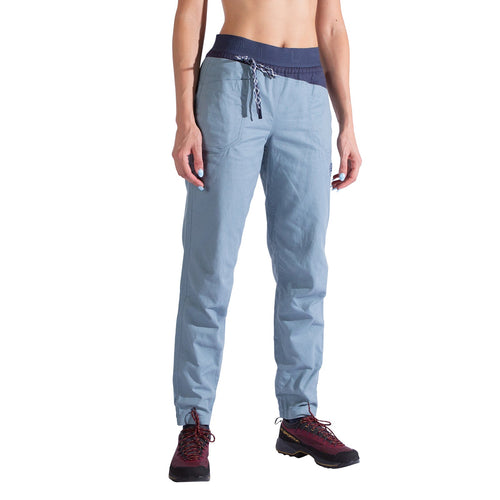 A person wearing La Sportiva Bolt Pants Women's in light blue organic cotton with an adjustable waistband and drawstring, paired with dark red hiking shoes. The photo is set against a plain white background.