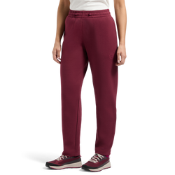 Vêtue d'un pantalon La Sportiva Podium pour femme de couleur bordeaux — de style pantalon de survêtement —, une personne se tient debout devant un fond blanc, ne laissant apparaître que le bas de son corps. Sa tenue est complétée par un haut blanc et des baskets bordeaux et noires.