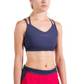 Une femme portant le La Sportiva Boulder Bra Women's en bleu marine et un short de sport rouge vif se tient debout sur un fond blanc. Son visage est partiellement hors du cadre.