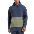 Un homme porte le sweat à capuche La Sportiva Podium Hoody pour homme, un sweat léger de sport bleu arborant le logo La Sportiva et doté d’une poche avant vert olive. Il se tient debout, face à l’objectif, une main le long du corps. Les cordons de la capuche pendent librement, mettant en valeur ce vêtement d’escalade confortable, idéal pour les activités sportives.