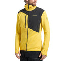 A man wears the La Sportiva Lucendro Thermal Hoody Men's, a yellow and black high-collar zip-up ideal as a thermal layer for mountaineers, while looking to his left against a plain white background.