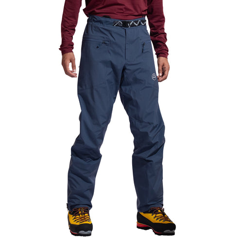 A person wearing La Sportiva Alpine Guide GTX Performance Pants Men's—waterproof, breathable pants with zippered pockets—is shown from the waist down, paired with yellow hiking boots, against a white background.