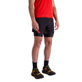 A person wearing a red shirt, La Sportiva Flow 5 Inch Shorts Men's (black with yellow accents), black socks, and black running shoes with yellow and red details, standing against a white background.