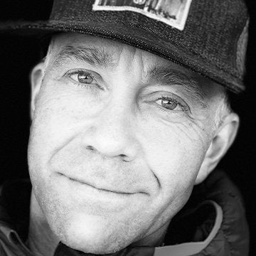 Black and white close-up of a person wearing a cap with a visible brand logo.
