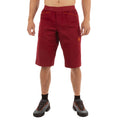 Une personne porte le short La Sportiva Flatanger Shorts Men's (2023) en rouge-orange, avec des chaussettes noires et des chaussures de trail noires avec des lacets orange, sur un fond blanc. Le mélange coton-spandex offre confort et flexibilité. La tête de la personne n'est pas visible.