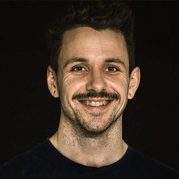 Man with a mustache smiling against a black background