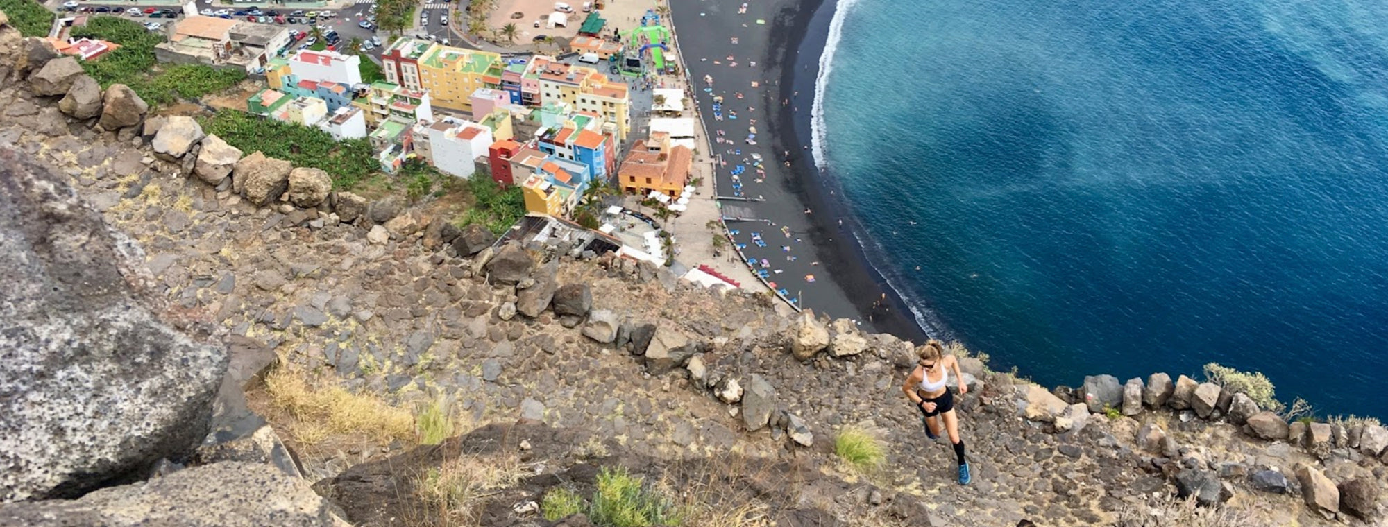 Person running along a coastal path with colorful buildings and blue ocean.