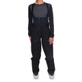 A woman models the La Sportiva Chaser EVO Shell Bib Pants with a high waist, paired with a long-sleeve black top and ski boots. She stands facing forward against a white background, arms relaxed and ready for snow adventures.
